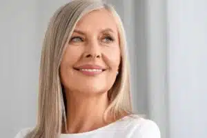 Smiling mature woman with smooth skin after facelift or neck lift, showcasing facial rejuvenation results.