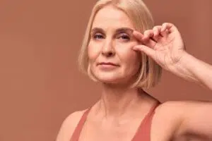 Mature woman gently lifting lower eyelid showing concern for dark circles and considering lower blepharoplasty.