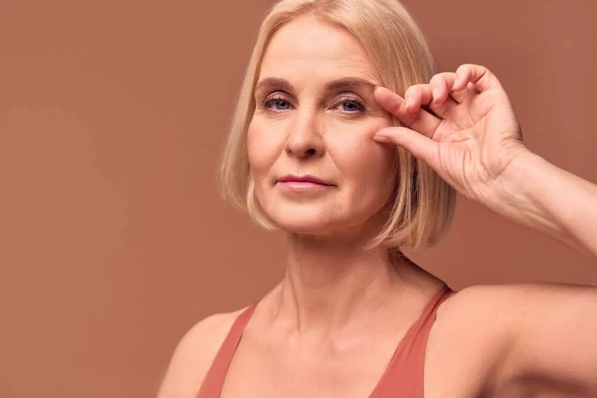 Mature woman gently lifting lower eyelid showing concern for dark circles and considering lower blepharoplasty.