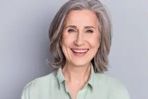 Smiling older woman with youthful eyes and smooth forehead, reflecting results of brow lift or blepharoplasty.